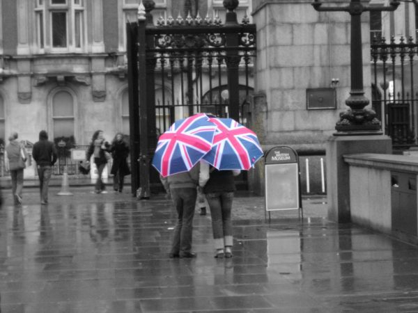 Man And Woman Standing In Front Of The British Museum With A British Flag Umbrella As It Is Raining.