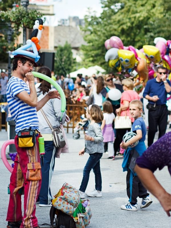 Man In Colourful Clothes Blowing Up Balloons While Busking As He Works and Travels Abroad.