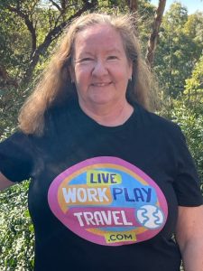 Sharyn McCullum In A Black T-shirt With Her Live Work Play Travel Logo In The Shape Of A World.